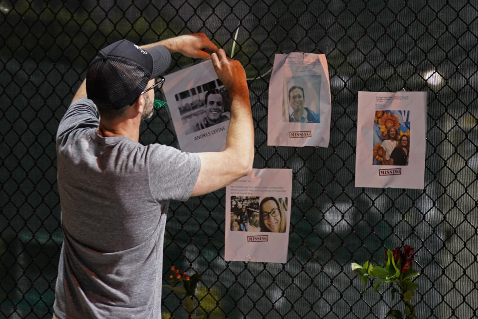 A man hangs a photo on a fence of someone missing near the site of an oceanfront condo building that partially collapsed in Surfside, Fla., Friday, June 25, 2021. (AP Photo/Gerald Herbert)