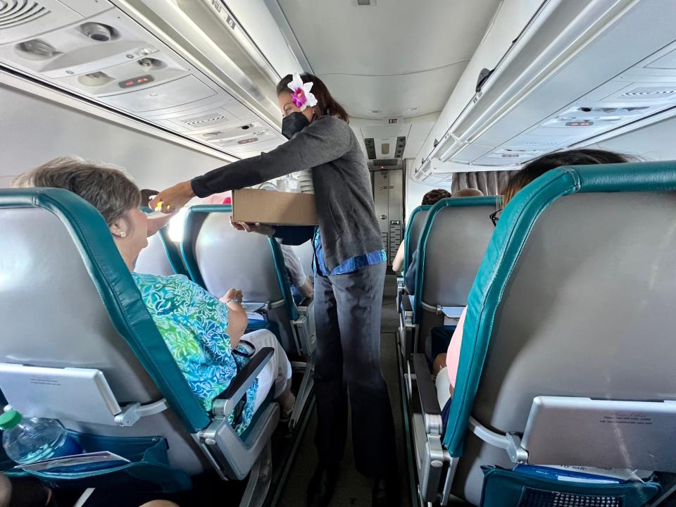 A flight attendant hands out snacks to passengers in aisle