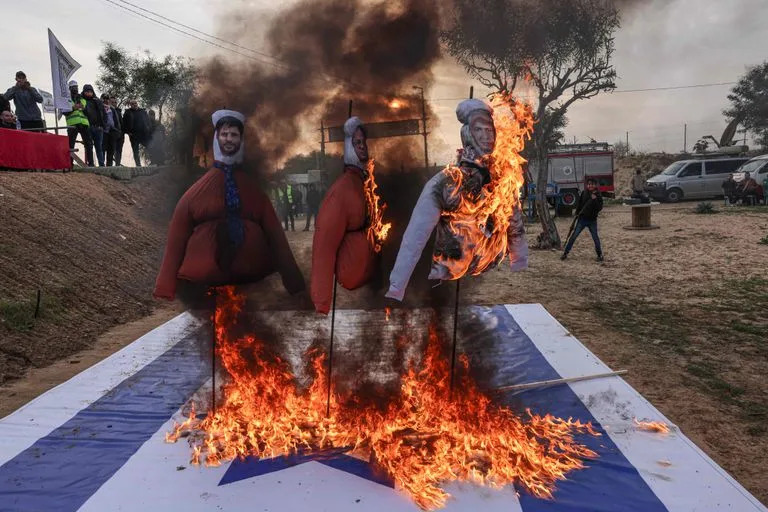 Militantes palestinos de la brigada Ansar, brazo militar del Movimiento por la Libertad de Palestina, queman la bandera israelí y efigies en las que aparecen el primer ministro israelí, Benjamin Netanyahu (dcha.), el nuevo ministro de Seguridad Nacional de Israel, Itamar Ben Gvir (cda.), y el líder del Partido Sionista Religioso de Israel, Bezalel Smotrich, durante un ejercicio militar en Jan Yunis, en el sur de la Franja de Gaza, el 1 de enero de 2023.