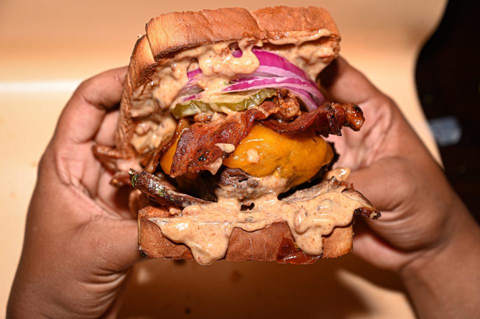 The Big Texas Brisket Burger at MilTex Kitchen features a cream cheese-stuffed burger, bacon jam aioli, braised brisket, red onions, pickles, and candied bacon and jalapeños. It's served on toasted Texas toast bread.