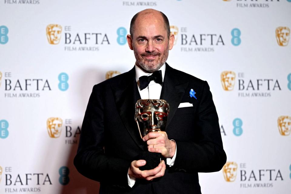 A man poses holding an award shaped like a mask.