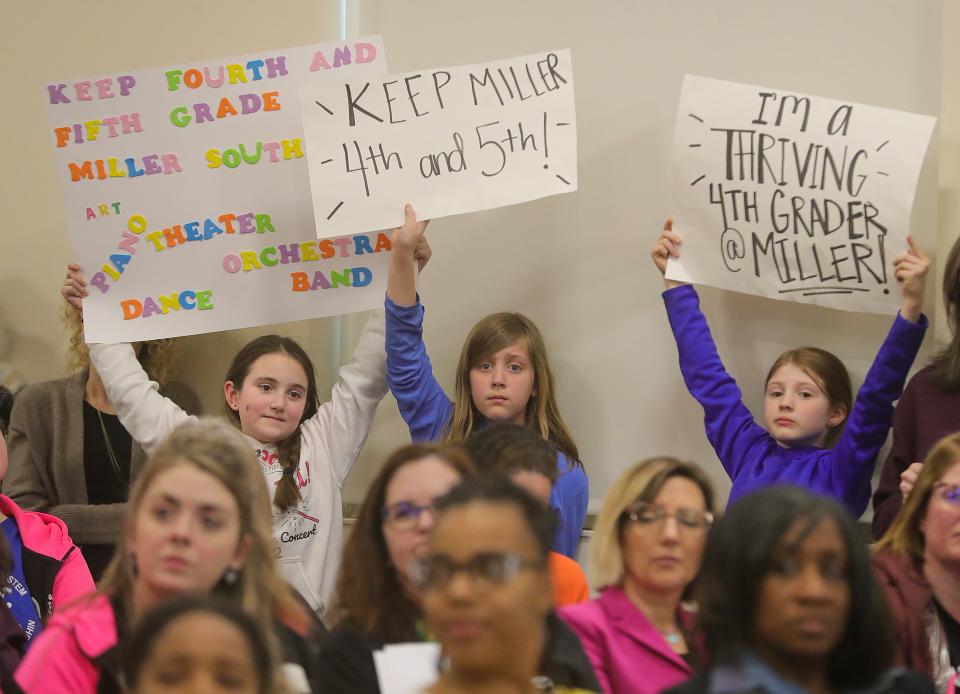 Miller South fourth grade students Sophie Smith, from left, Alanna Powers, and Emery Swiger hold signs during a special meeting discussing long-term facilities plans Monday in Akron.