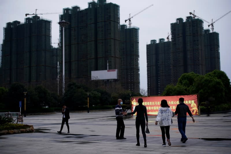 People with face masks are seen at a square with a propaganda sign near residential buildings under construction in Xianning