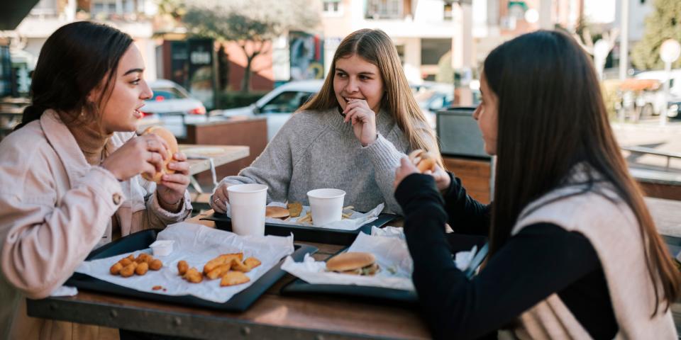 Group of Gen Z teenagers drinking and eating food together sat outside