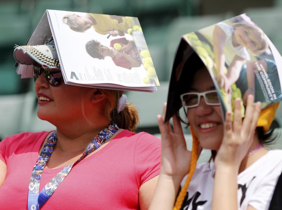 Fans sheild themselves from the sun using programmes at the Wimbledon Tennis Championships in London