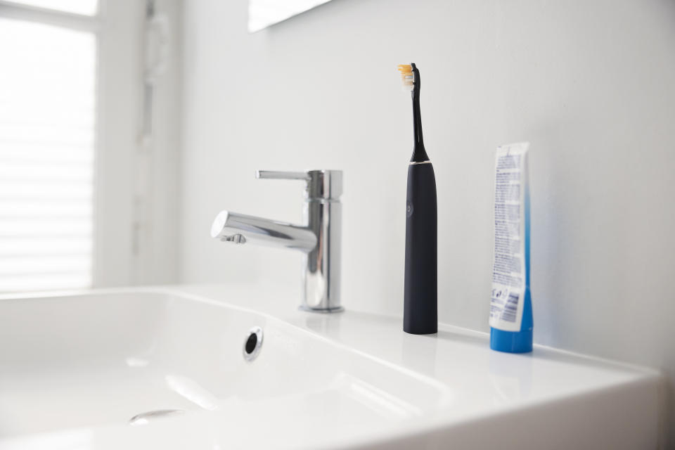 A bathroom sink with a chrome faucet, an electric toothbrush and a tube of toothpaste on the shelf