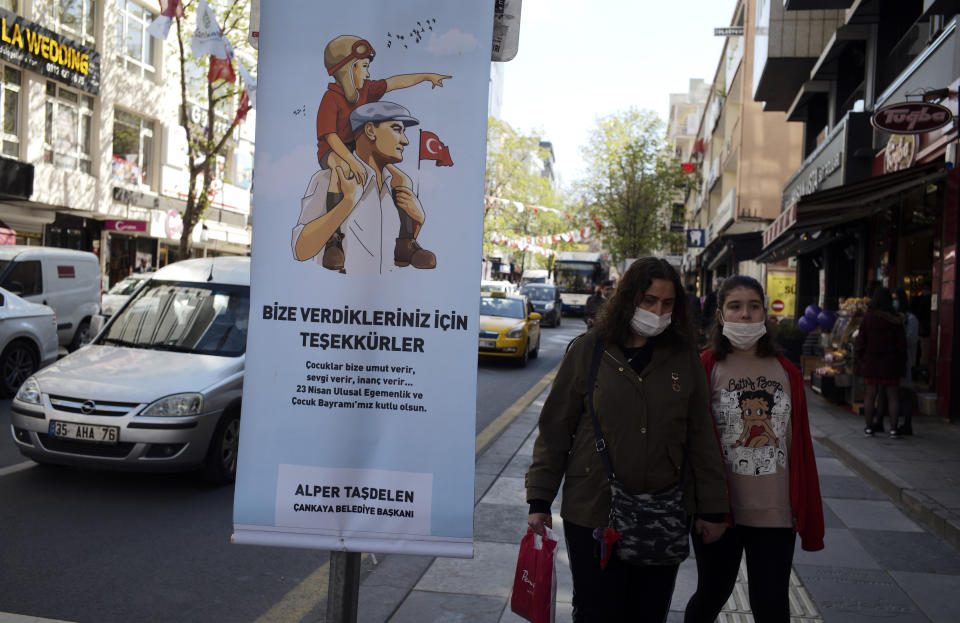 People wearing masks to help protect against the spread of coronavirus, walk along a busy street before a nationwide lockdown, in Ankara, Turkey, Thursday, April 22, 2021. Turkey has announced that it is extending an upcoming weekend lockdown to include a public holiday on Friday, as it grapples with soaring infections. The country has been posting record-high levels of infections and deaths since it eased COVID-19 restrictions in early March. The poster is depicting Turkey's founder Kemal Ataturk holding a child.(AP Photo/Burhan Ozbilici)