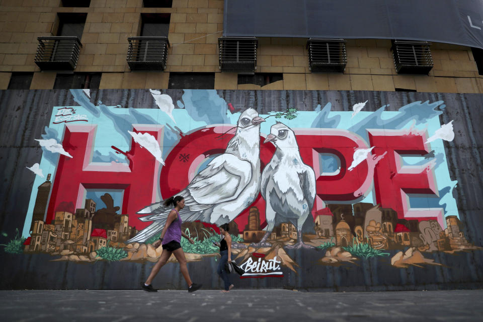 Women walk past a graffiti "Hope" painted on metals barrier that closed the entrance of a hotel that was damaged by Aug. 4 explosion that hit the seaport of Beirut, Lebanon, Monday, Oct. 12, 2020. A year ago, hundreds of thousands of Lebanese took to the streets in protests nationwide that raised hopes among many for a change in a political elite that over that decades has run the country into the ground. (AP Photo/Bilal Hussein)