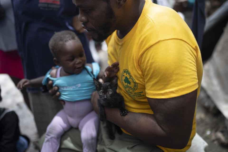 Jean-Kere Almicar holds a cat and a baby, in the yard of his home, in Port-au-Prince, Haiti, Sunday, June 4, 2023. Almicar, who once lived in Scranton, Pennsylvania but moved back to Haiti in 2007, uses his own money to help feed people displaced by gang violence who have sought refuge in his front yard. (AP Photo/Ariana Cubillos)