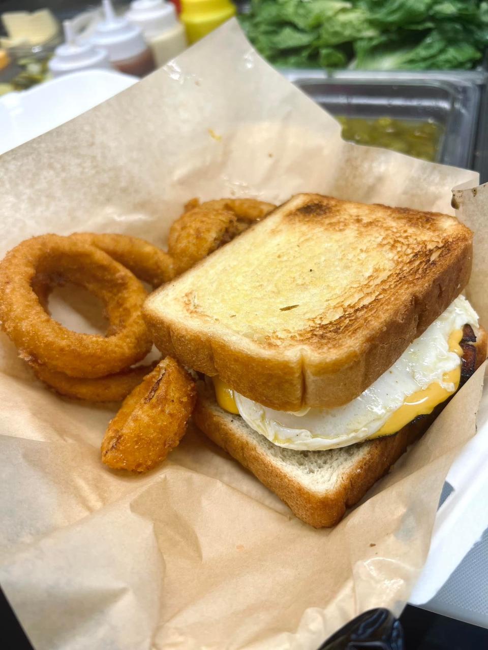 The Top Bun Cougar is a smoked fried bologna topped with a fried egg, American cheese, mayo and mustard served on Texas toast. All entrées are served with one side, such as these hand breaded onion rings.