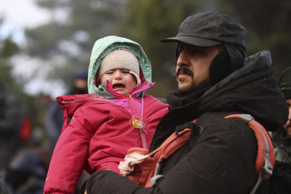 A man carries a child as he gathers with other migrants at the Belarus-Poland border near Grodno, Belarus, Monday, Nov. 8, 2021. Poland increased security at its border with Belarus, on the European Union's eastern border, after a large group of migrants in Belarus appeared to be congregating at a crossing point, officials said Monday. The development appeared to signal an escalation of a crisis that has being going on for months in which the autocratic regime of Belarus has encouraged migrants from the Middle East and elsewhere to illegally enter the European Union, at first through Lithuania and Latvia and now primarily through Poland. (Leonid Shcheglov/BelTA via AP)