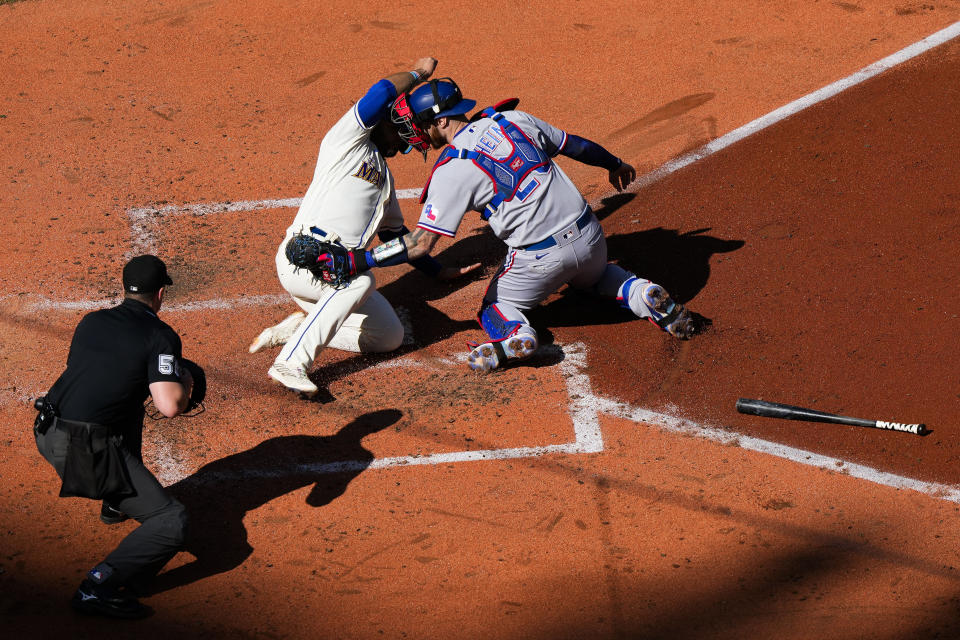 Texas Rangers catcher Jonah Heim, right, cannot get a tag on Seattle Mariners' Eugenio Suárez, center, at home plate, allowing Suárez to score on a groundout from Dominic Canzone (not shown), during the fourth inning of a baseball game Sunday, Oct. 1, 2023, in Seattle. (AP Photo/Lindsey Wasson)