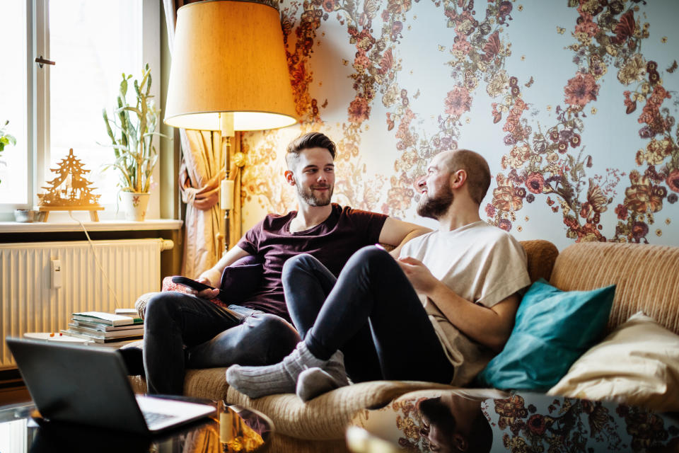 A gay couple sat on their couch, chatting while watching tv together at home.
