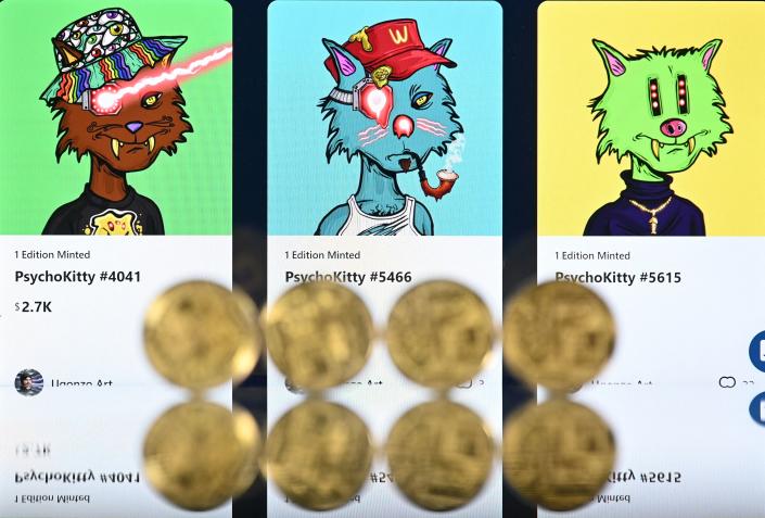An illustration picture taken in London on December 30, 2021, shows gold plated souvenir cryptocurrency coins arranged beside a screen displaying a Crypto.com NFT (Non-Fungible Token) marketplace showing three PsychoKitty NFTs created by psychedelic artist Ugonzo. - Non-fungible tokens or NFTs are cryptographic assets stored on a blockchain with unique identification metadata that distinguish them from each other. - RESTRICTED TO EDITORIAL USE - MANDATORY MENTION OF THE ARTIST UPON PUBLICATION - TO ILLUSTRATE THE EVENT AS SPECIFIED IN THE CAPTION (Photo by Justin TALLIS / AFP) / RESTRICTED TO EDITORIAL USE - MANDATORY MENTION OF THE ARTIST UPON PUBLICATION - TO ILLUSTRATE THE EVENT AS SPECIFIED IN THE CAPTION / RESTRICTED TO EDITORIAL USE - MANDATORY MENTION OF THE ARTIST UPON PUBLICATION - TO ILLUSTRATE THE EVENT AS SPECIFIED IN THE CAPTION (Photo by JUSTIN TALLIS/AFP via Getty Images)