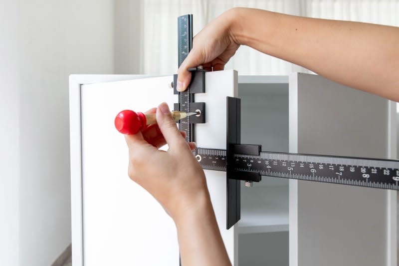 Using a sharp point to mark where the hardware holes should go in a cabinet door, with the cabinet hardware jig serving as a guide