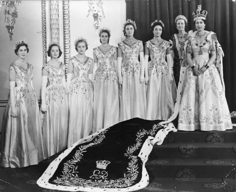 La Reina usando la túnica de terciopelo carmesí en la sala del trono del Palacio de Buckingham el día de su coronación, con las doncellas de honor a su lado. (Getty Images)