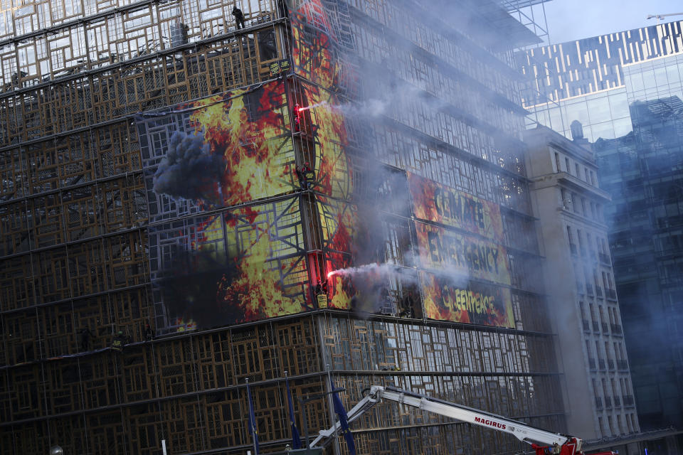 Climate activists set off smoke as they climb next to a giant banner on the Europa building during a demonstration outside an EU summit meeting in Brussels, Thursday, Dec. 12, 2019. Greenpeace activists on Thursday scaled the European Union's new headquarters, unfurling a huge banner warning of a climate emergency hours before the bloc's leaders gather for a summit focused on plans to combat global warming.(AP Photo/Francisco Seco)