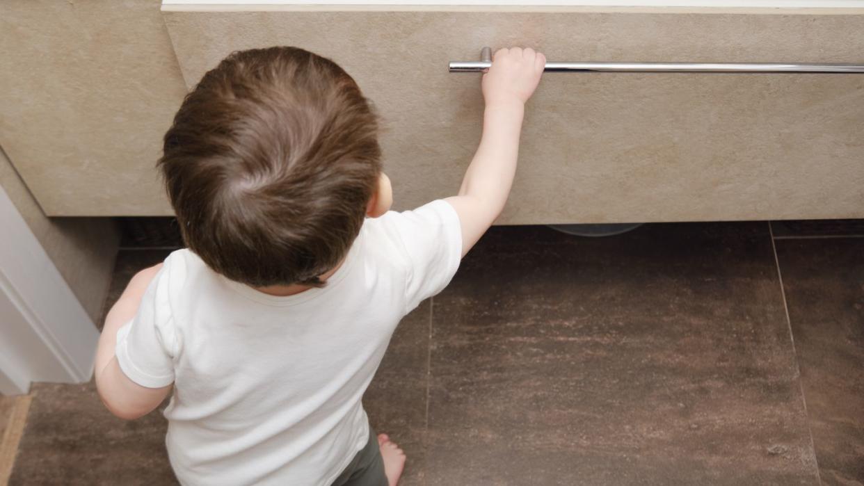 toddler baby pulls out an item drawer in a home bathroom a small child explores the closet in the bathroom kid aged one year eight months