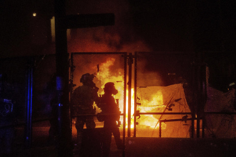 Federal officers guard the Mark O. Hatfield U.S. Courthouse as a fire lit by protesters burns on the other side of a perimeter fence Saturday, July 25, 2020, in Portland, Ore. On the streets of Portland, a strange armed conflict unfolds night after night. It is raw, frightening and painful on both sides of an iron fence separating the protesters on the outside and federal agents guarding a courthouse inside. This weekend, journalists for The Associated Press spent the weekend both outside, with the protesters, and inside the courthouse, with the federal agents, documenting the fight that has become an unlikely centerpiece of the protest movement gripping America. (AP Photo/Noah Berger)