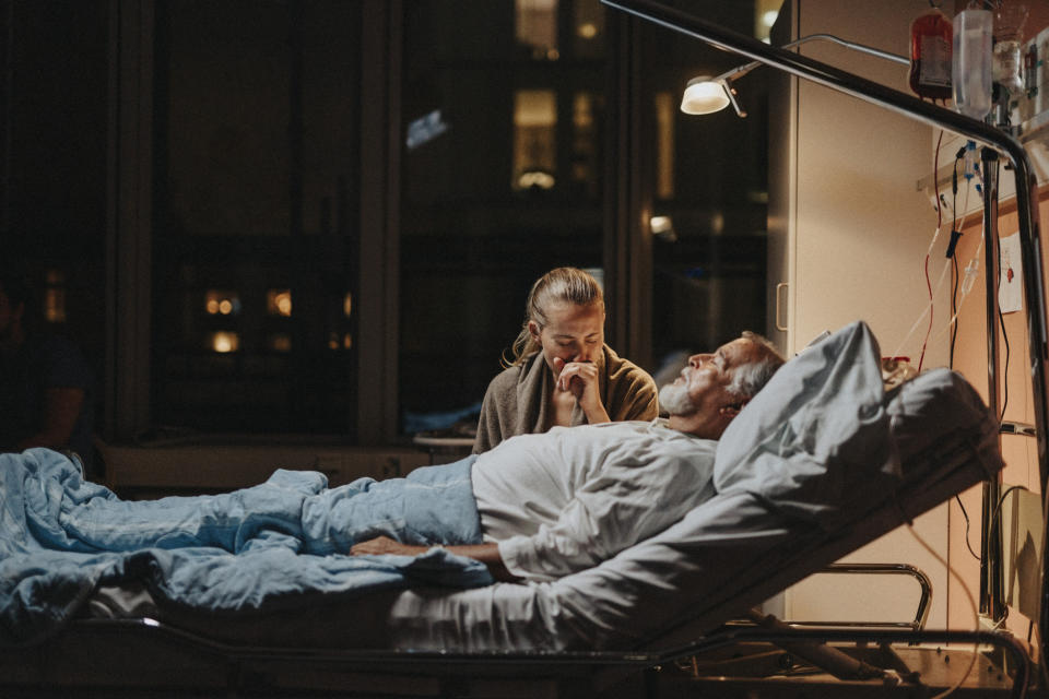 woman holding the hand of a man in a hospital bed