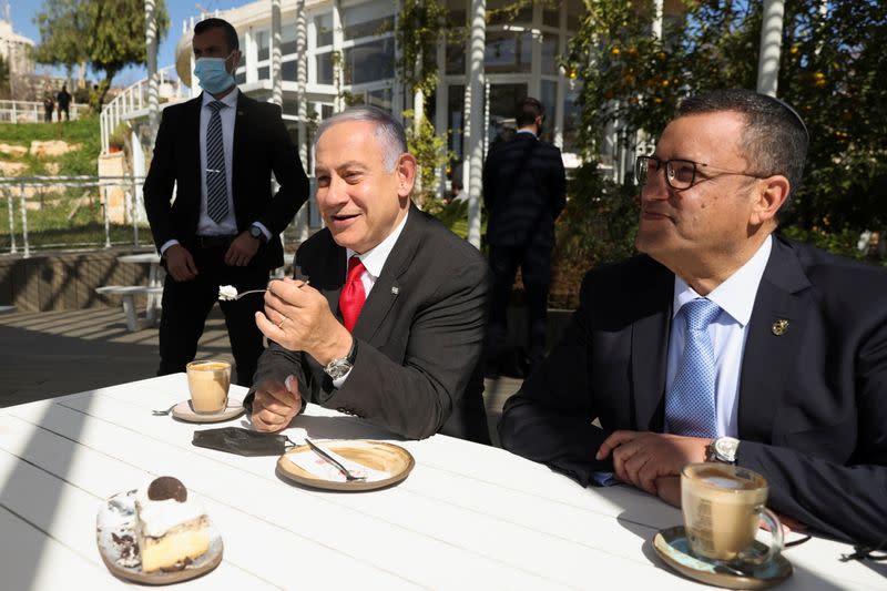 Israeli Prime Minister Benjamin Netanyahu eats a piece of cake as he sits with Jerusalem Mayor, Moshe Leon, at a cafe while Israel further eases coronavirus disease (COVID-19) restrictions in Jerusalem