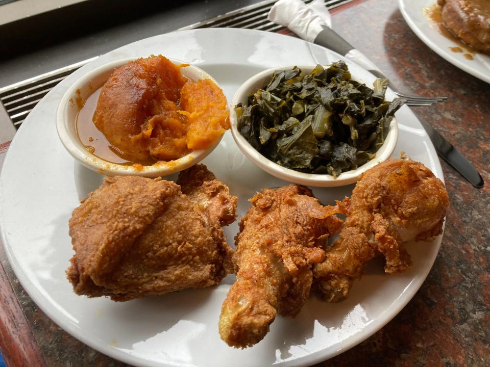 Three pieces of juicy fried chicken with sides of collard greens and candied yams.