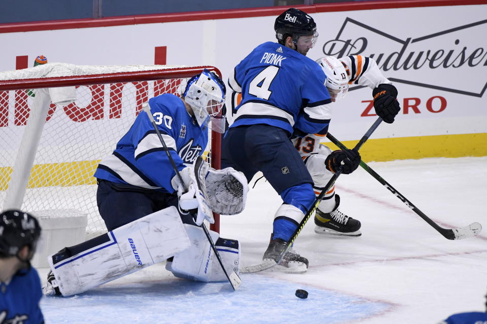 Winnipeg Jets goaltender Laurent Brossoit (30) makes a save on Edmonton Oilers' Jesse Puljujarvi (13) as Neal Pionk (4) defends during the second period of an NHL hockey game, Sunday, Jan. 24, 2021 in Winnipeg, Manitoba. (Fred Greenslade/The Canadian Press via AP)