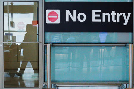 FILE PHOTO: International travelers (reflected in a closed door) arrive on the day that U.S. President Donald Trump's limited travel ban, approved by the U.S. Supreme Court, goes into effect, at Logan Airport in Boston, Massachusetts, U.S., June 29, 2017. REUTERS/Brian Snyder/File Photo