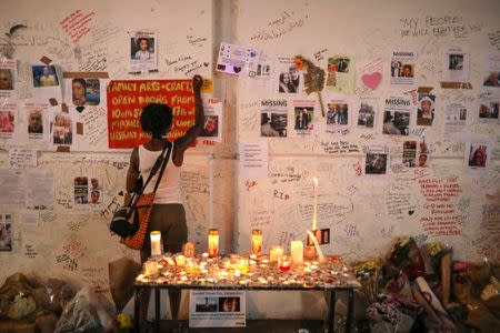 FILE PHOTO: A woman writes on a wall covered with tributes to and pictures of the victims of the Grenfell apartment tower fire in North Kensington, London, Britain, June 18, 2017. REUTERS/Marko Djurica/File Photo