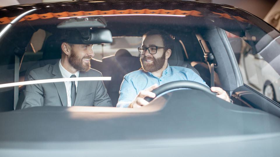 Sales manager with a young client inspecting vehicle interior at the car dealership, view through the windshield.