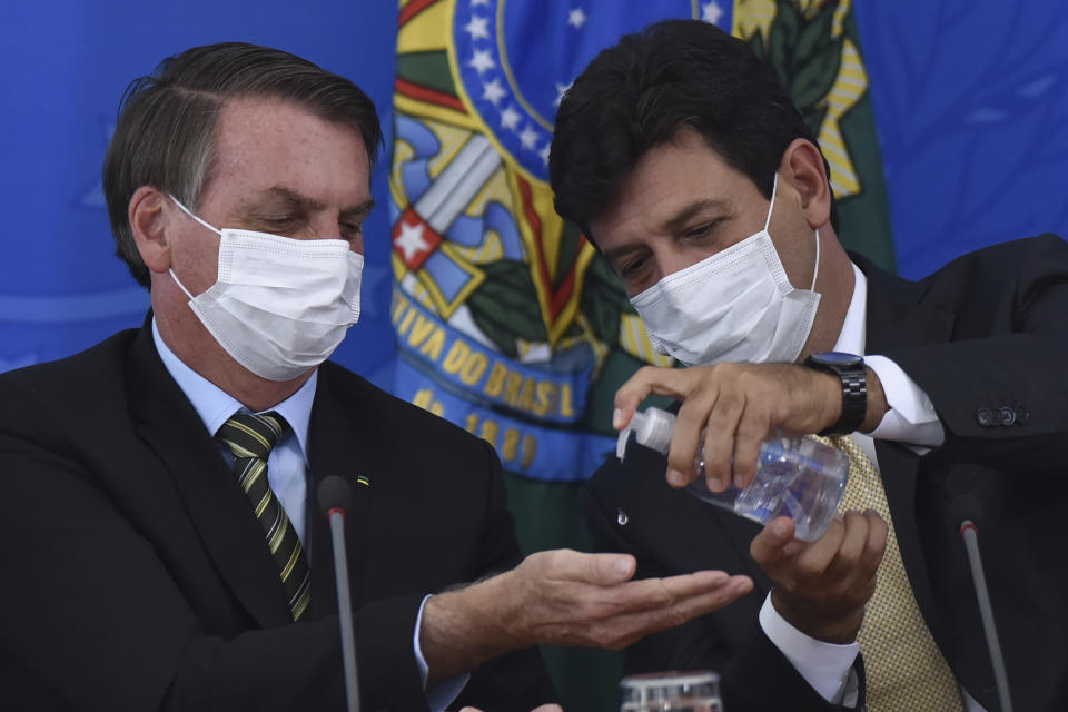 Wearing masks, Brazil's Health Minister Luiz Henrique Mandetta, right, applies alcohol gel on hands of President Jair Bolsonaro's hands during a press conference on the new coronavirus, at the Planalto Presidential Palace in Brasilia, Brazil, Wednesday, March 18, 2019. For most people COVID-19 causes mild or moderate symptoms. For others, especially the elderly and people with existing health problems, it can cause many other serious illnesses, including pneumonia. (AP Photo/Andre Borges)