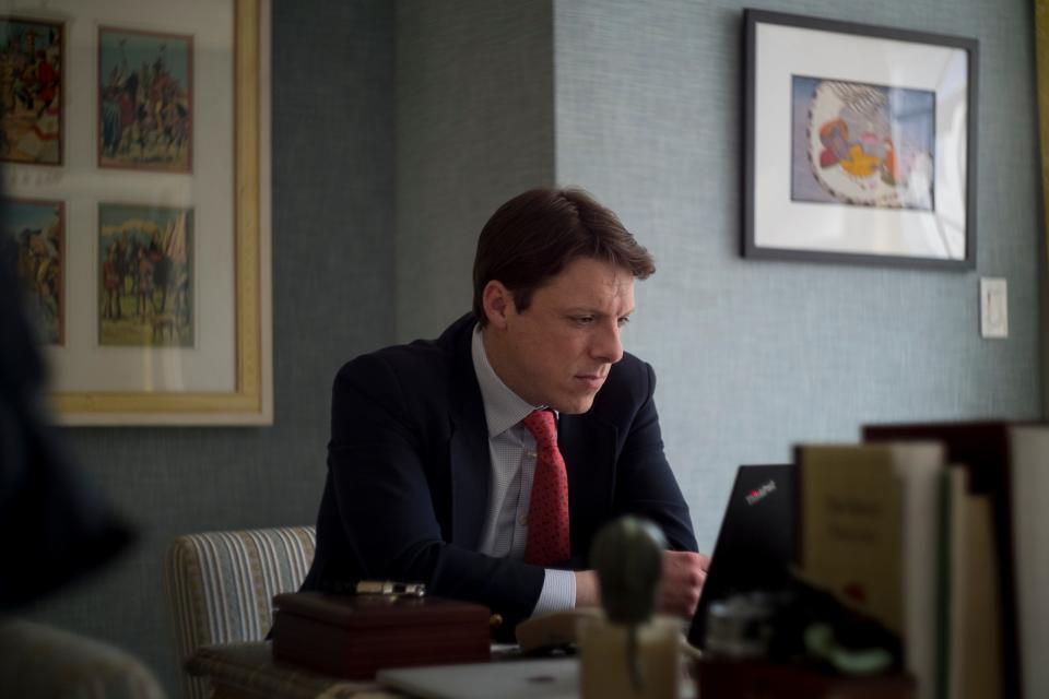 A man in a suit works at a desk on a laptop.