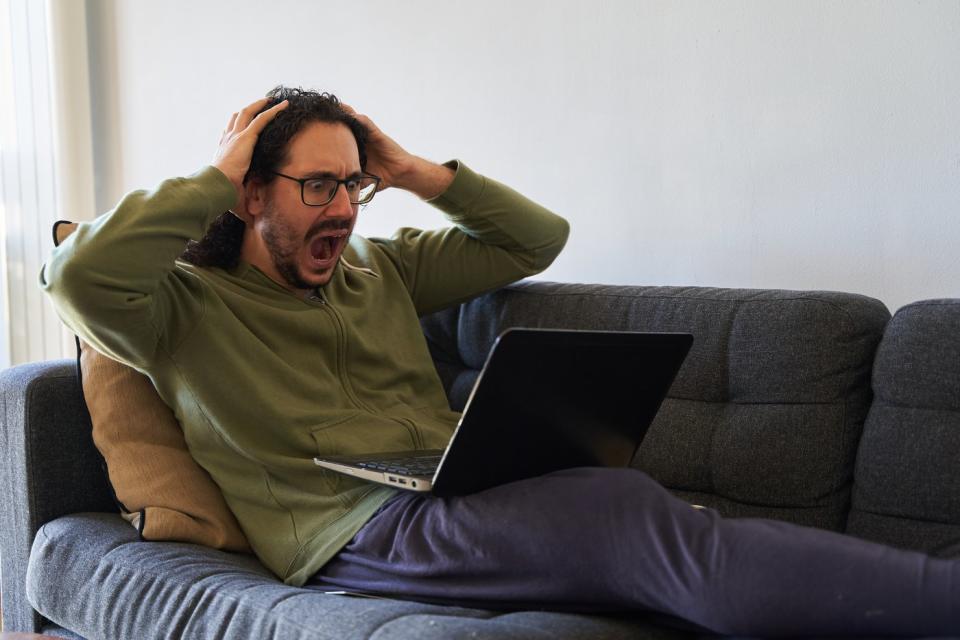 Someone stretched out on a couch while looking at their computer with an exasperated expression on their face.