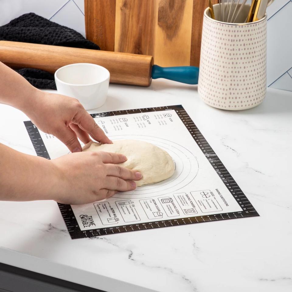 Hands pressing dough on a printed pastry mat with size guides for rolling