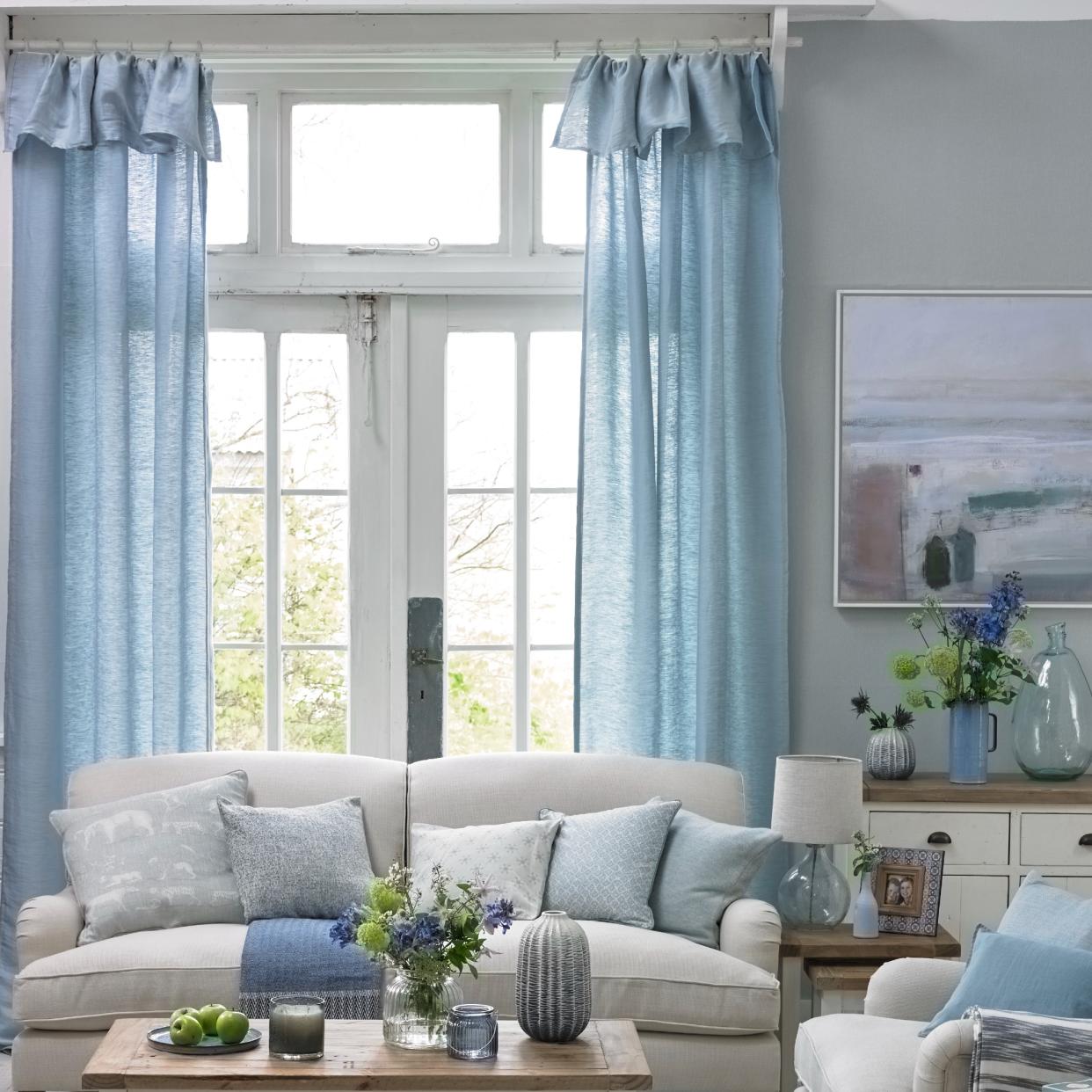  A living room with high ceilings and window covered by long blue curtains. 
