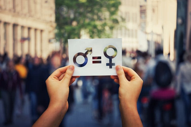 Woman's hands and white sheet of paper with male and female symbol on crowded city street background