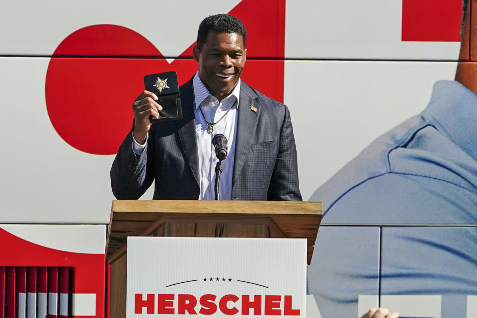 FILE - Herschel Walker, Republican candidate for U.S. Senate in Georgia, flashes a police badge as he speak to supporters during a campaign rally Oct. 18, 2022, in Atlanta. Walker campaigns for the U.S. Senate as a champion of free enterprise and advocate for the mentally ill, felons and others. And the Georgia Republican has called for policies that blend those priorities. Yet Walker, through a major chicken processor that he touts as a principal partner to one of his primary businesses, has benefited from years of unpaid labor by drug offenders routed to the facility by Oklahoma state courts.(AP Photo/John Bazemore, File)