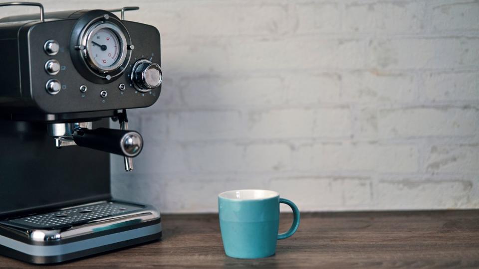 An espresso machine and coffee mug on a wooden countertop  in front of a brick wall