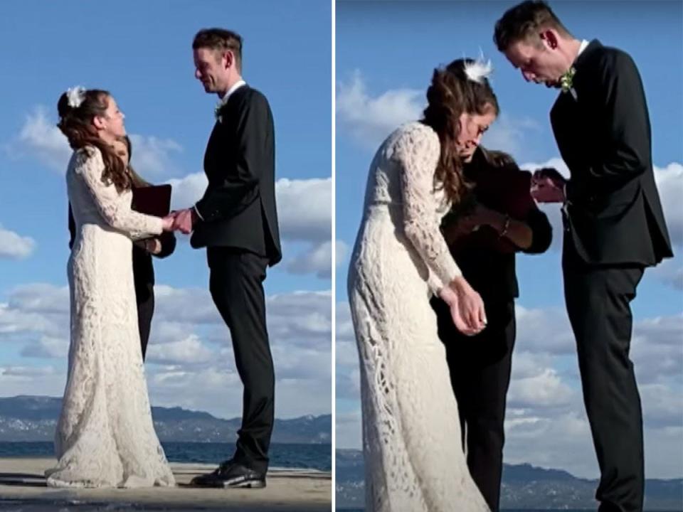 A bride and groom stand on a dock as the groom drops a wedding ring into a lake.