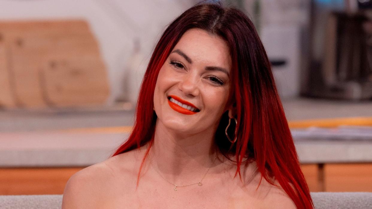 Dianne Buswell similing on couch in off shoulder top