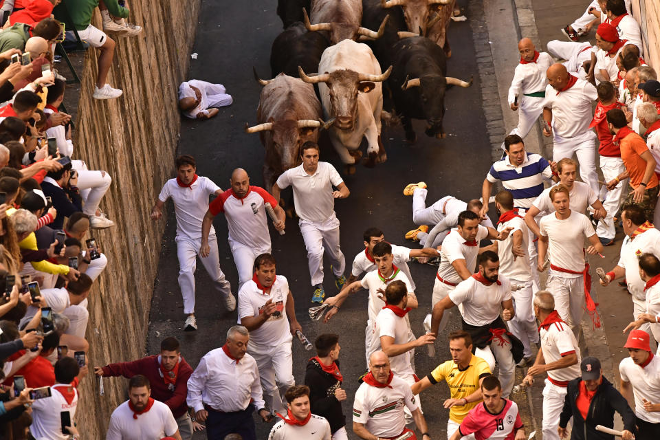 People run through the street with fighting bulls at the San Fermin Festival in Pamplona, northern Spain, Friday, July 8, 2022. Revellers from around the world flock to the city every year for nine days of uninterrupted partying in Pamplona's famed running of the bulls festival which was suspended for the past two years because of the coronavirus pandemic. (AP Photo/Alvaro Barrientos)