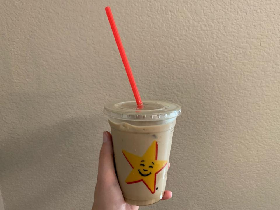 a hand holding Carl's Jr iced coffee in front of a beige wall