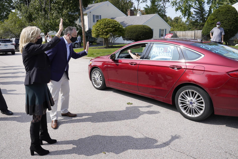 Jill Biden, left, wife of Democratic presidential candidate former vice president Joe Biden, and Doug Emhoff, center, husband of Democratic vice presidential candidate Sen. Kamala Harris, D-Calif., greet a supporter in a passing car during a campaign stop, Wednesday, Sept. 16, 2020, in Manchester, N.H. (AP Photo/Steven Senne)