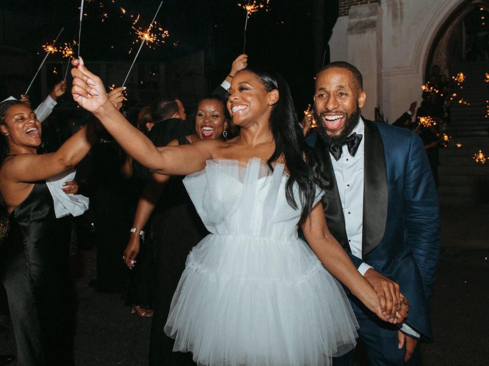 A bride and groom smile as they raise sparklers with their guests on their wedding day.