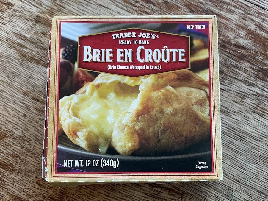 Box of Trader Joe's Brie en croute with a picture of oozing baked Brie on the package placed on a wooden counter