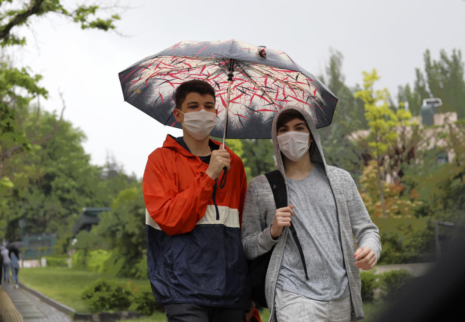 People wearing face masks for protection against the new coronavirus, walk in rain just hours before a four-day new curfew declared by the government in an attempt to control the spread of coronavirus, in Ankara, Turkey, Friday, May 22, 2020. The country has opted to impose short weekend and holiday curfews, instead of full lockdowns, fearing possible negative effects on the already troubled economy. (AP Photo/Burhan Ozbilici)