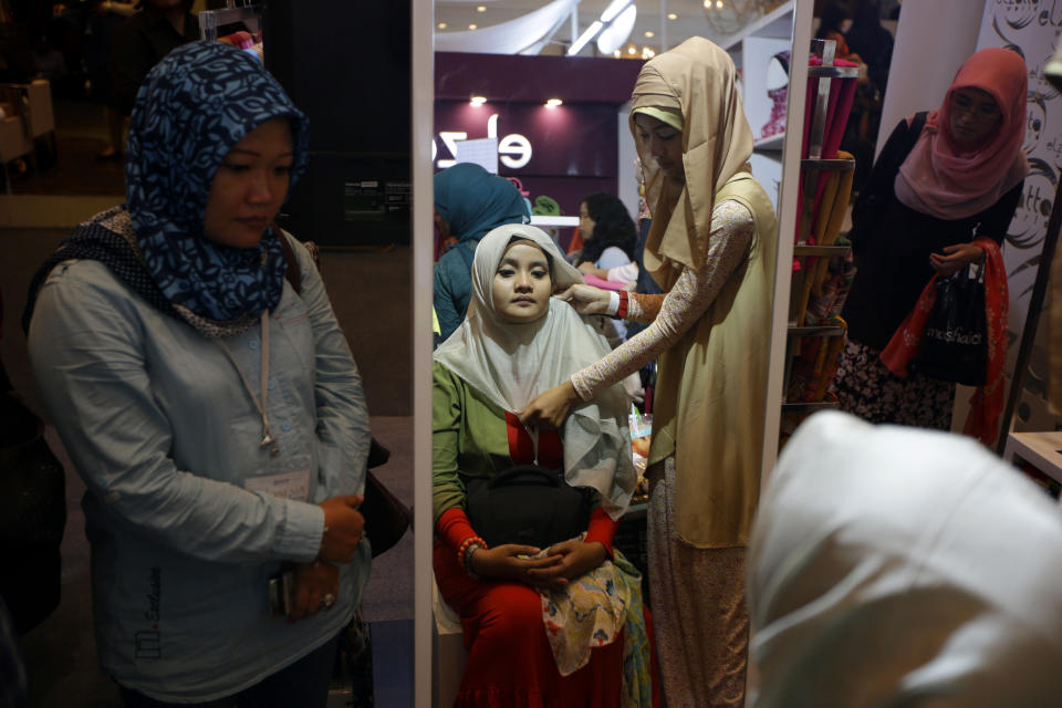 In this Thursday, May 30, 2013, an Indonesian Muslim woman tries on a headscarf during Islamic Fashion Fair in Jakarta, Indonesia. Indonesia is the world's most populous Muslim country, but most people follow a moderate form of the religion. Many women wear bright and creative headscarves along with brand-name jeans and long-sleeved fitted shirts. (AP Photo/Dita Alangkara)