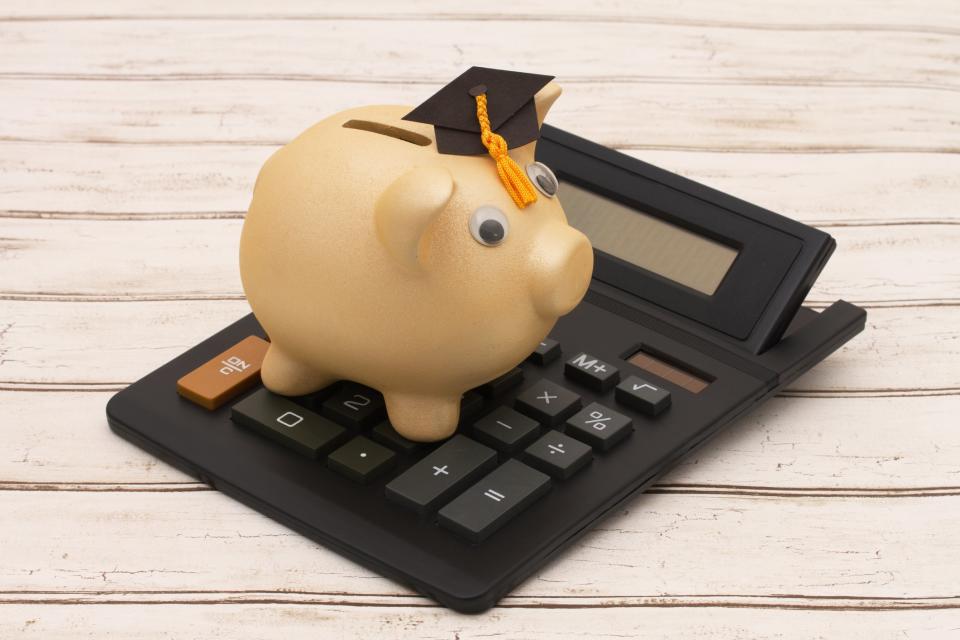 A piggy bank wearing a graduation cap sits on top of a calculator.