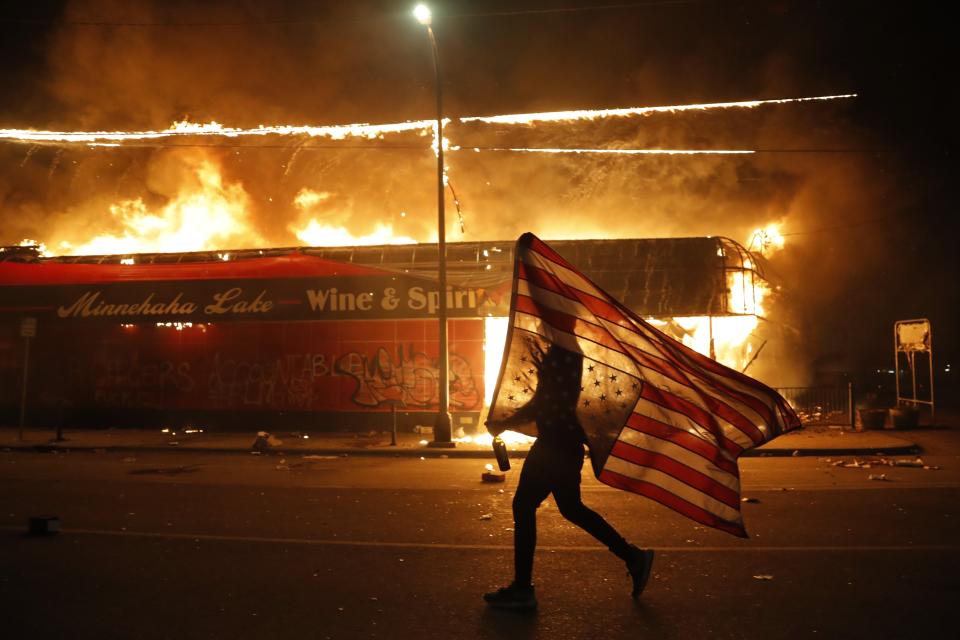 FILE - In this May 28, 2020, file photo, a protester carries a American flag upside down, a sign of distress, next to a burning building in Minneapolis. Former Minneapolis police Officer Derek Chauvin faces decades in prison when he is sentenced Friday, June 25, 2021, following his murder and manslaughter convictions in the death of George Floyd. A new exhibition of photographs owned by Elton John opens this week at London’s Victoria and Albert Museum. It includes more than 300 pieces by 140 photographers selected from the vast collection of John and his husband David Furnish. (AP Photo/Julio Cortez, File)