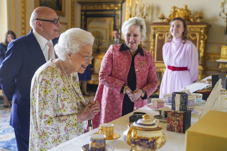 FILE - Britain's Queen Elizabeth II views a display of artefacts to commemorate the 70th anniversary of British craftwork company, Halcyon Days, in the White Drawing Room at Windsor Castle, Windsor, England, Wednesday March 23, 2022. Britain is getting ready for a party featuring mounted troops, solemn prayers — and a pack of dancing mechanical corgis. The nation will celebrate Queen Elizabeth II’s 70 years on the throne this week with four days of pomp and pageantry in central London. (Steve Parsons/Pool via AP)